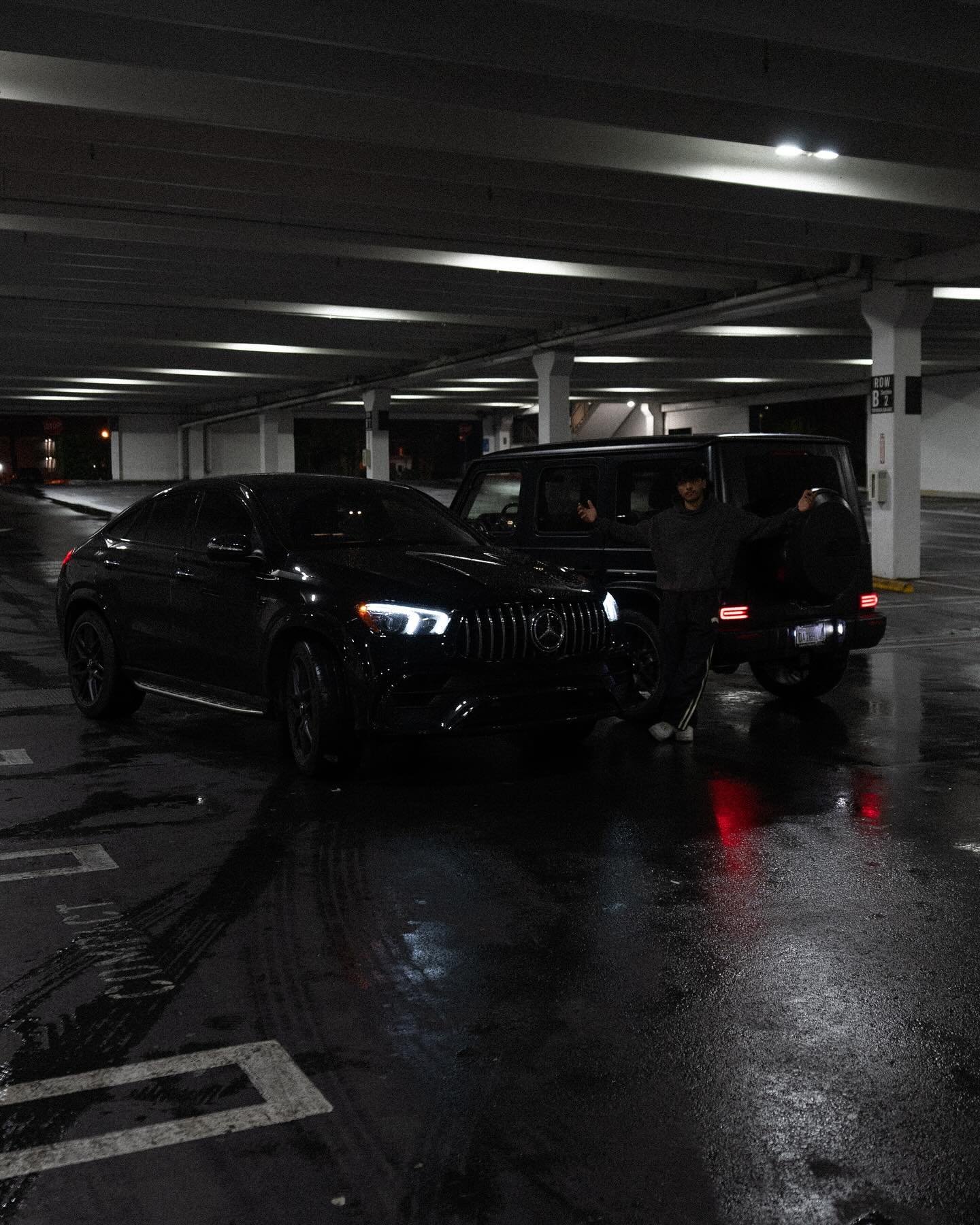Sharif standing between two black Mercedes vehicles in a parking garage